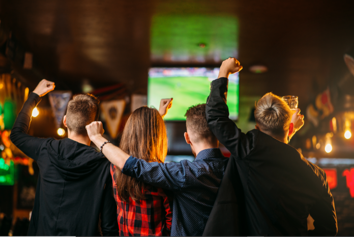 imagem mostra grupo de pessoas assistindo uma partida de futebol.